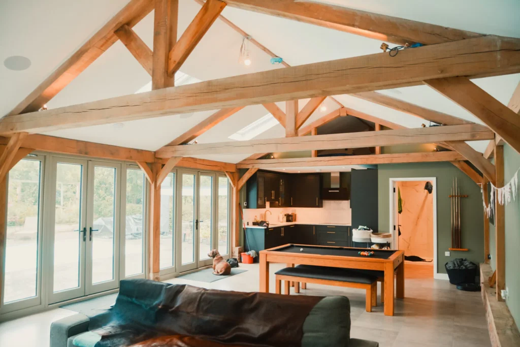 Interior view of a modern oak frame extension featuring a spacious kitchen and dining area, showcasing the timber structure and large windows, located in Kent.